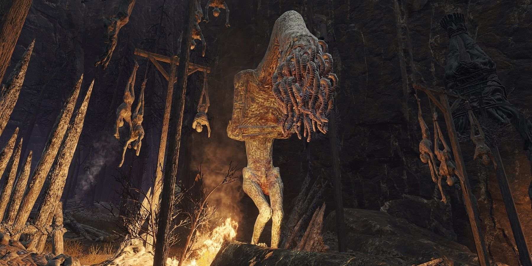 Elden Ring Lesser Wormface stands next to hanging corpses and fire.