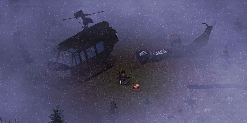 The player sitting by a campfire, fog and snow all around them. Behind them is a down helicopter.