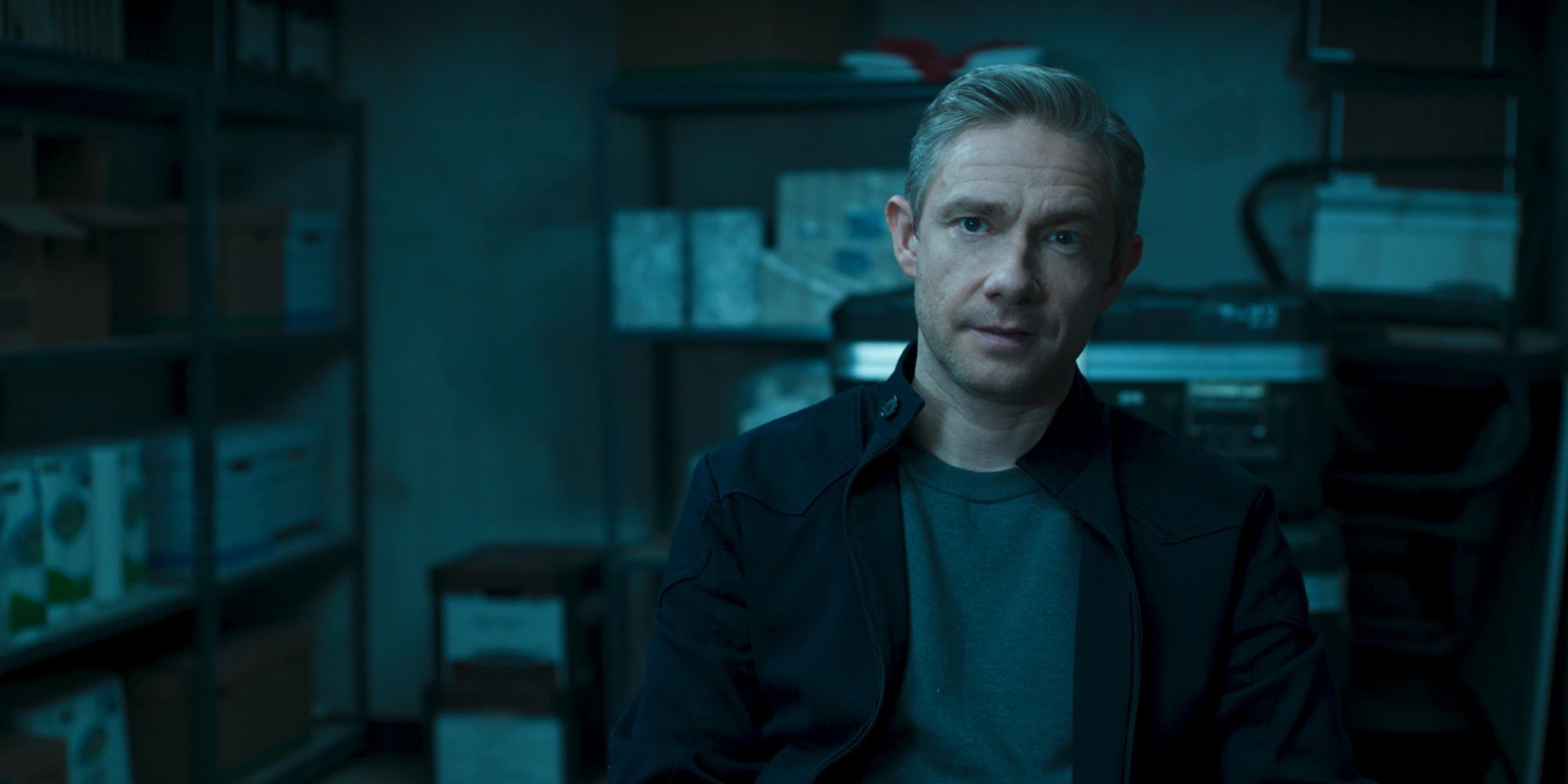 Still of Martin Freeman as Everett Ross wearing a dark jacket and gray shirt sitting in a storage room in Black Panther