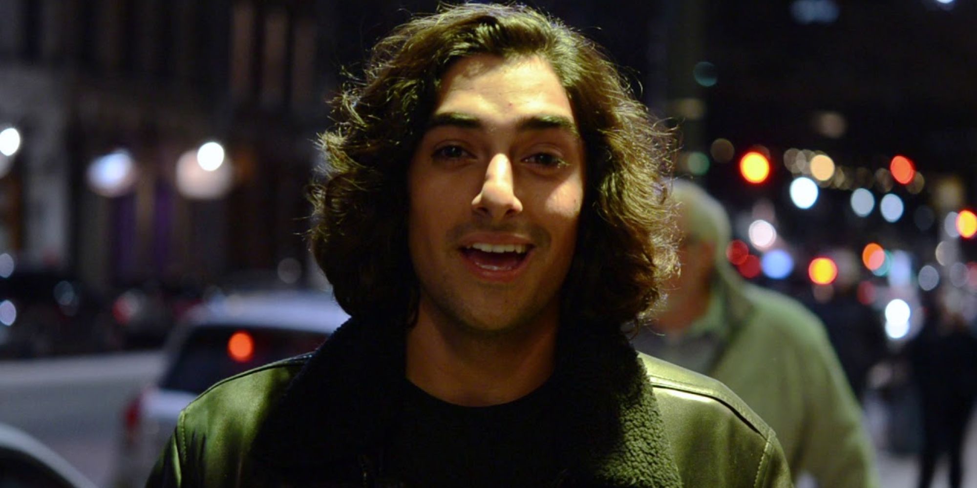Still of actor Eman Esfandi standing on a busy street at night