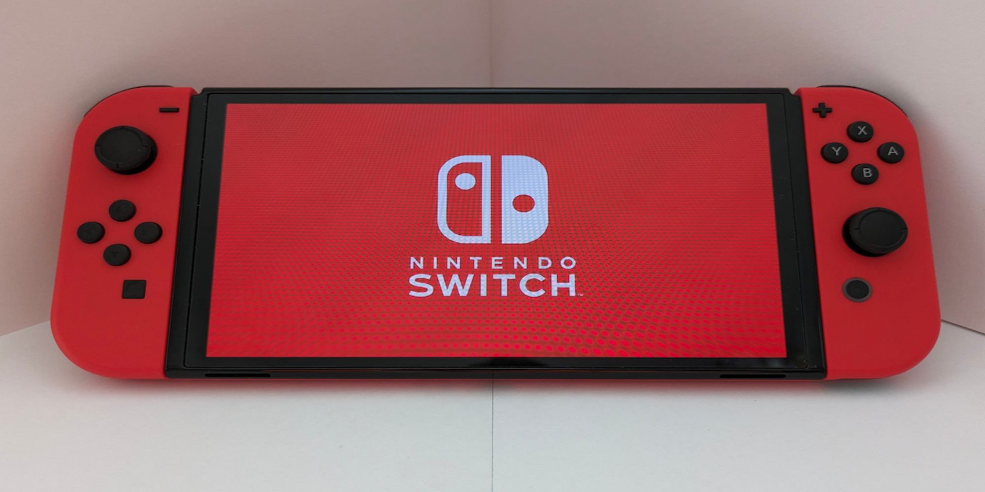 A red nintendo switch resting on a white wall